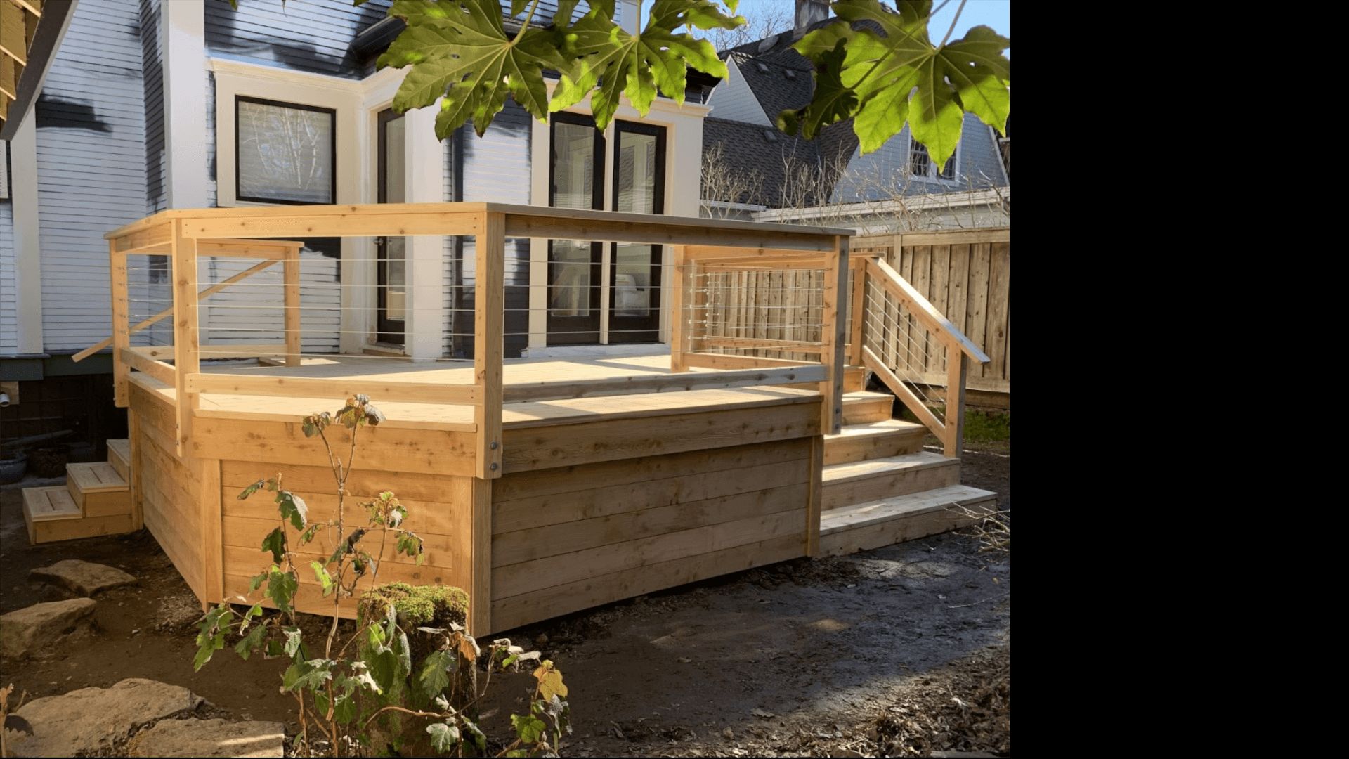 Raised cedar deck with cable railing beside a white house