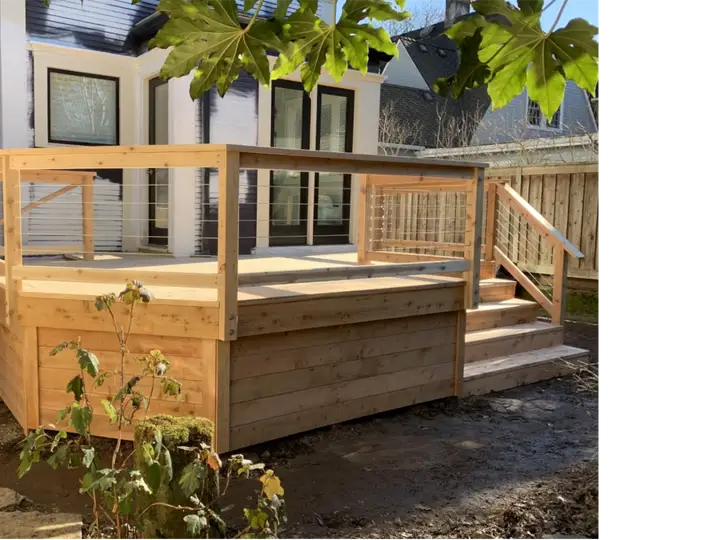 Raised cedar deck with horizontal cable railing beside a white house