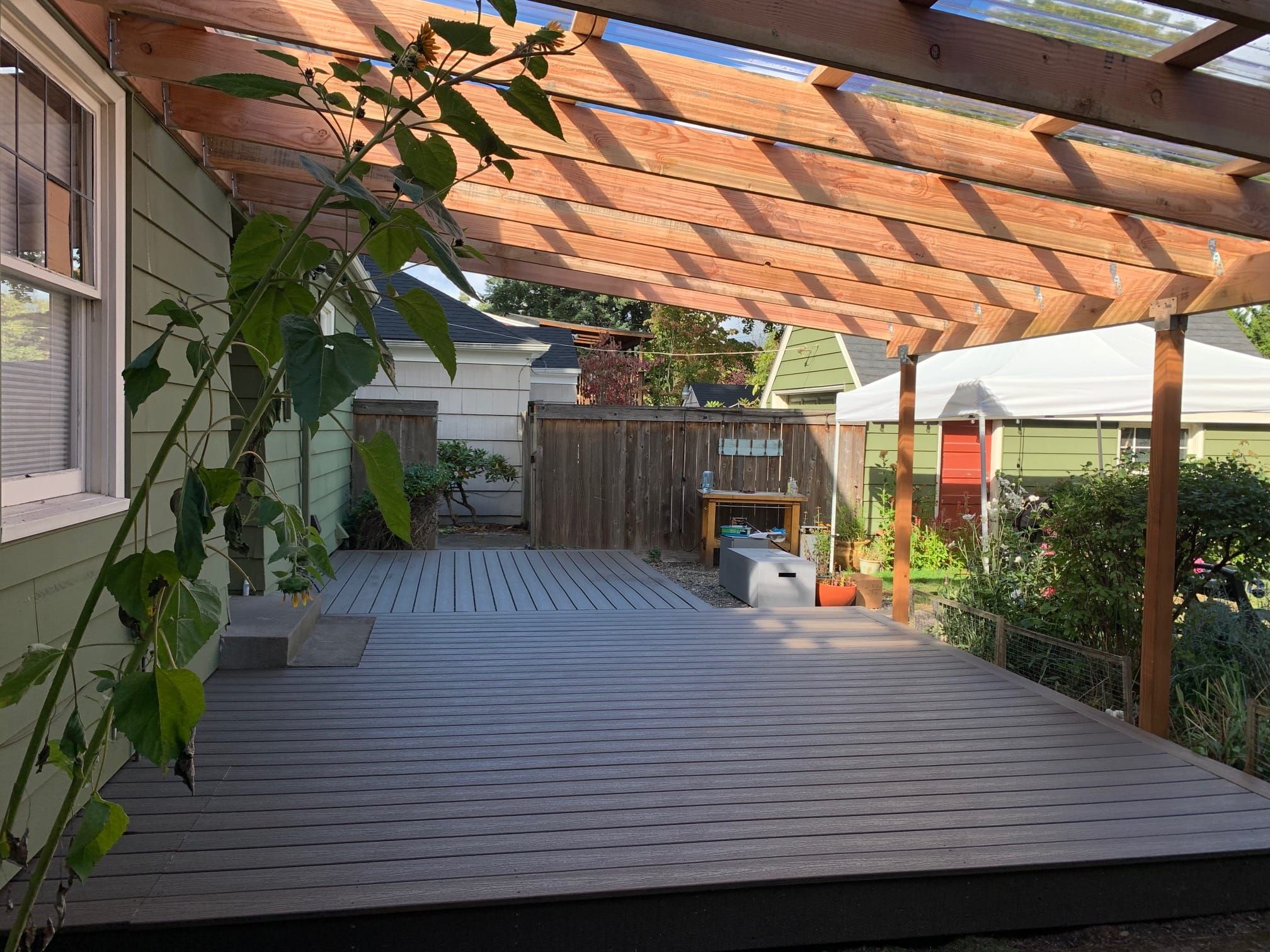 Gray composite deck under a cedar pergola beside a house