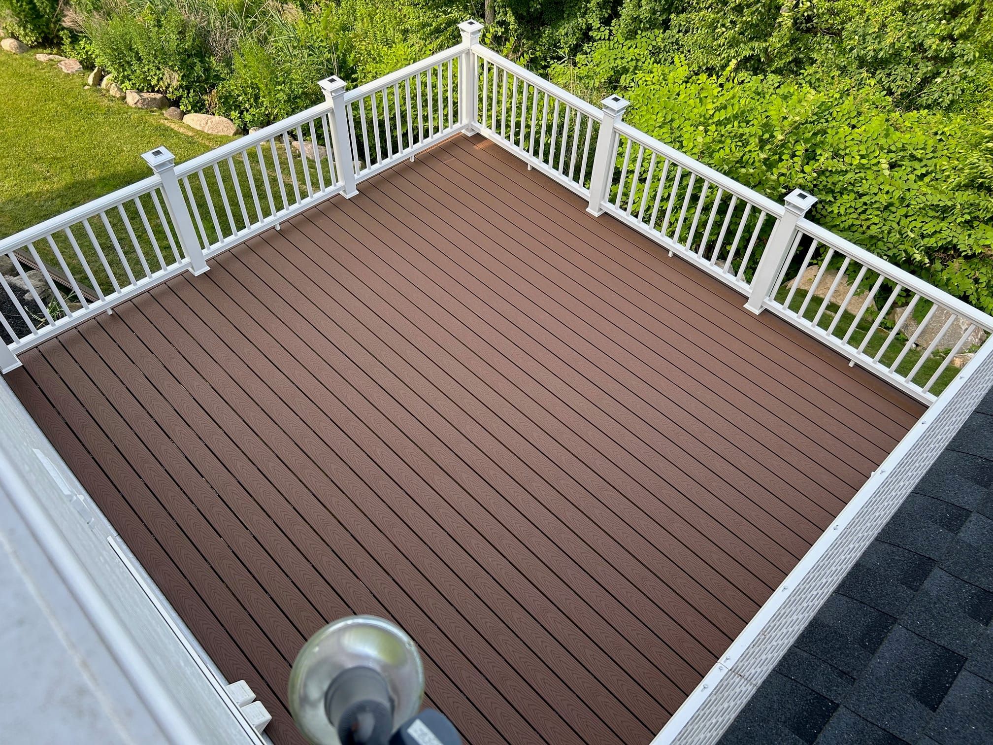 Elevated chestnut-brown composite deck with white railings above a green yard